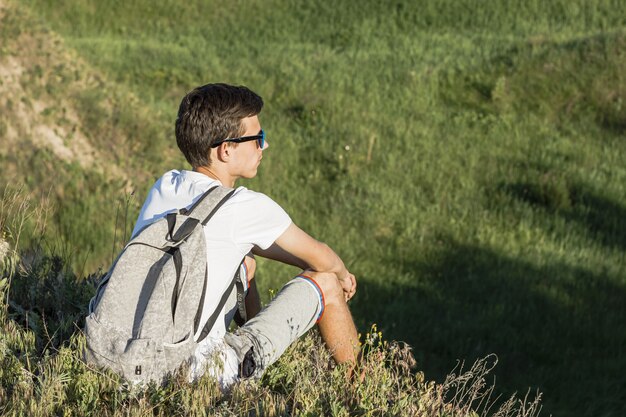 Giovane che si siede e che gode della vista verde