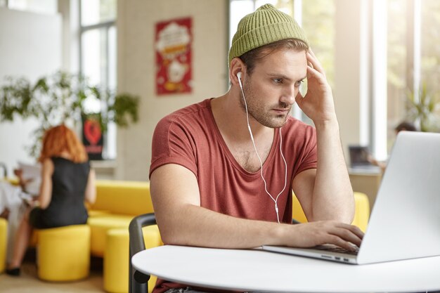 Giovane che si siede nella caffetteria con il computer portatile