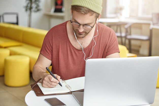 Giovane che si siede nella caffetteria con il computer portatile