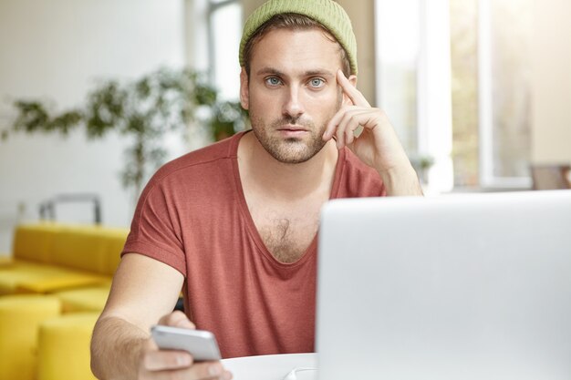 Giovane che si siede nella caffetteria con il computer portatile