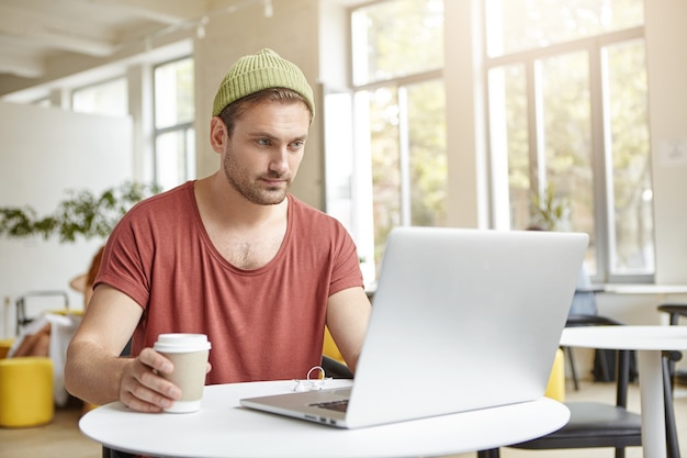 Giovane che si siede nella caffetteria con il computer portatile