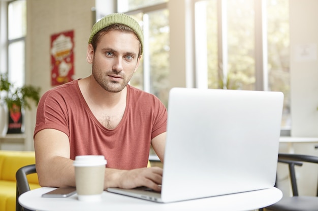 Giovane che si siede nella caffetteria con il computer portatile