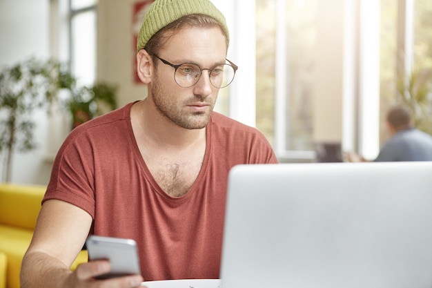 Giovane che si siede nella caffetteria con il computer portatile