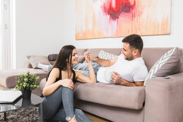 Giovane che si trova sulla mano della holding del sofà della sua amica che si siede sulla terra