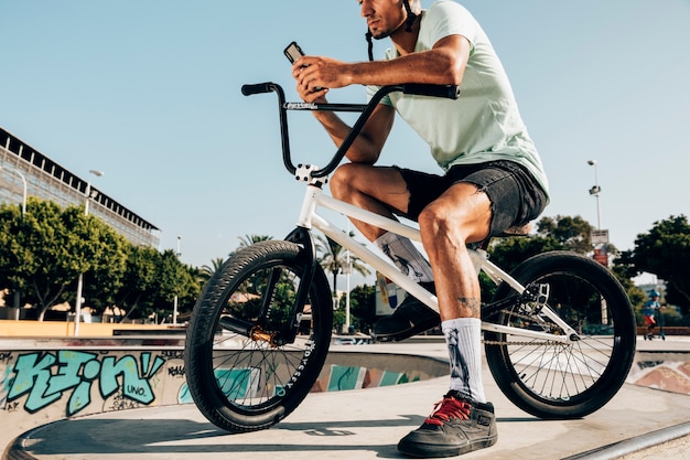 Giovane che sta sulla bici del bmx che esamina il telefono