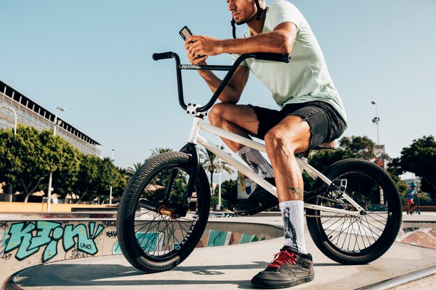 Giovane che sta sulla bici del bmx che esamina il telefono