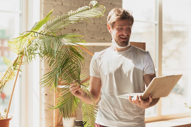 Giovane che studia a casa durante i corsi online per giardiniere, biologo, fiorista. Ottenere la professione mentre si è isolati, mettere in quarantena contro la diffusione del coronavirus. Utilizzando laptop, smartphone, cuffie.