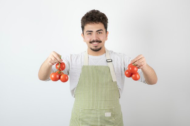 Giovane che tiene i pomodori freschi con la mano e sorride alla macchina fotografica.