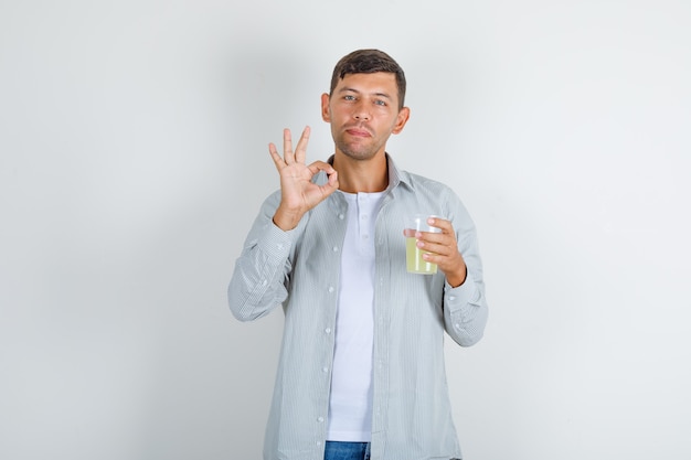 Giovane che tiene il bicchiere di succo con il segno giusto in camicia