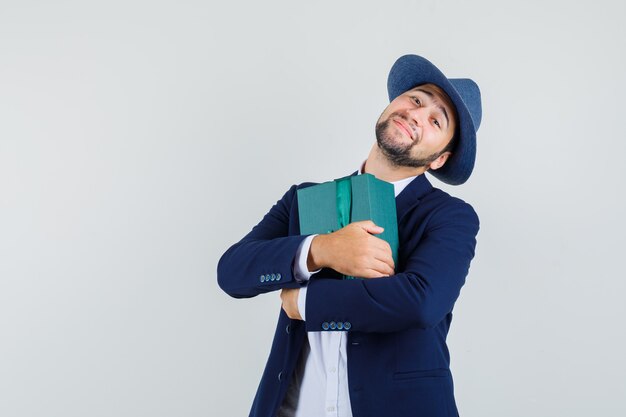 Giovane che tiene la casella attuale in vestito, cappello e che sembra felice. vista frontale.