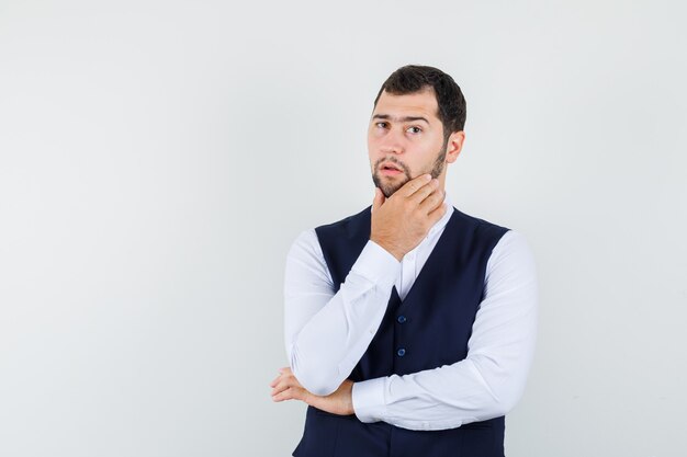 Giovane che tiene la mano sul mento in camicia, gilet e guardando pensieroso