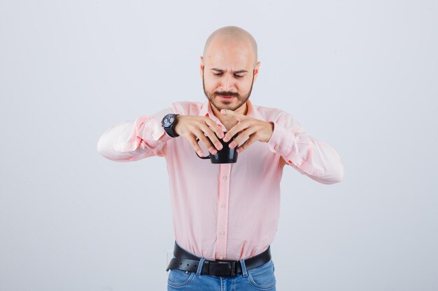 Giovane che tiene tazza piena di tè caldo in camicia rosa, jeans, vista frontale.