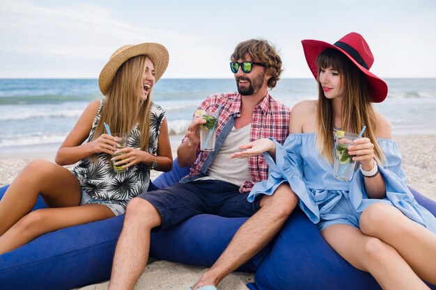 Giovane compagnia hipster di amici in vacanza al bar sulla spiaggia, bevendo cocktail mojito, felice positivo, stile estivo, sorridendo felice, due donne e un uomo che si divertono insieme, parlando, flirtare, romanticismo, tre