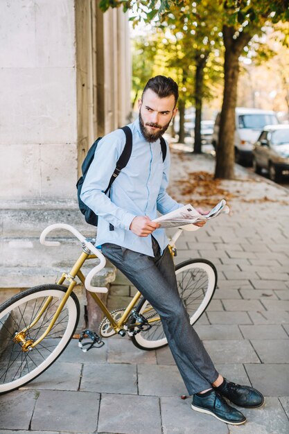 Giovane con il giornale che si appoggia sulla bicicletta