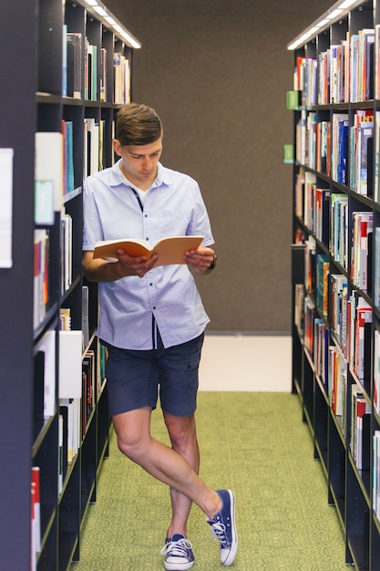 Giovane con il libro che si appoggia sullo scaffale per libri