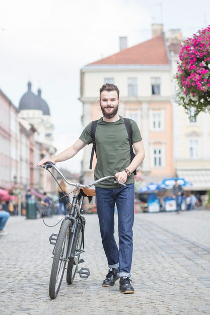 Giovane con la bicicletta che cammina sulla strada