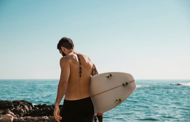 Giovane con tavola da surf vicino oceano