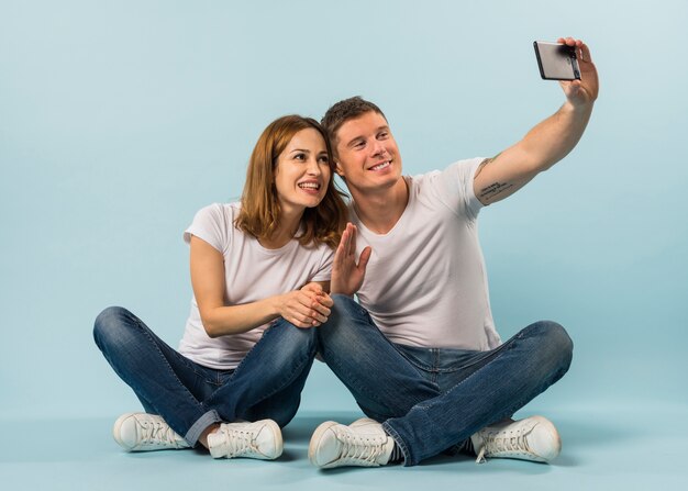 Giovane coppia agitando la mano prendendo selfie su smartphone contro il contesto blu