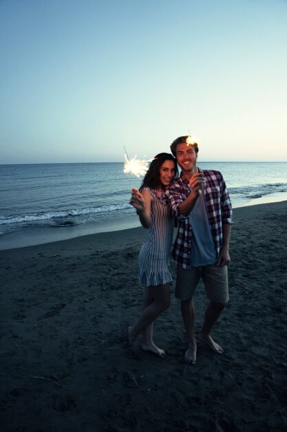 Giovane coppia con sparkler in una spiaggia di tramonto
