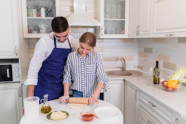 Giovane coppia di pasta di rotolamento per pizza in cucina