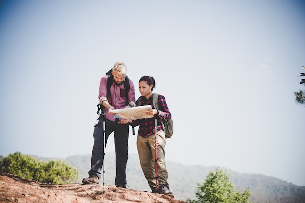 Giovane coppia di turisti che viaggiano in vacanza in montagna guardando la mappa in cerca di attrazioni. Concetto di viaggio.