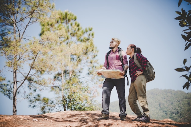 Giovane coppia di turisti che viaggiano in vacanza in montagna guardando la mappa in cerca di attrazioni. Concetto di viaggio.