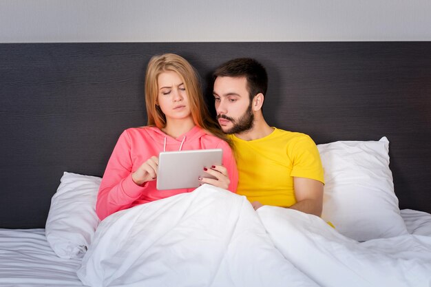 Giovane coppia dolce sul letto a guardare qualcosa su Tablet Gadget. Concetto di tecnologia e persone