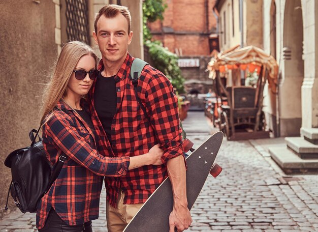 Giovane coppia hipster, bel pattinatore e la sua ragazza che si coccolano in piedi su una strada della vecchia Europa.