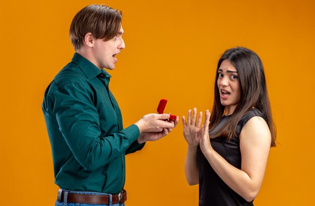 Giovane coppia il giorno di San Valentino ragazzo arrabbiato che dà la fede nuziale a una ragazza scontenta isolata su sfondo arancione