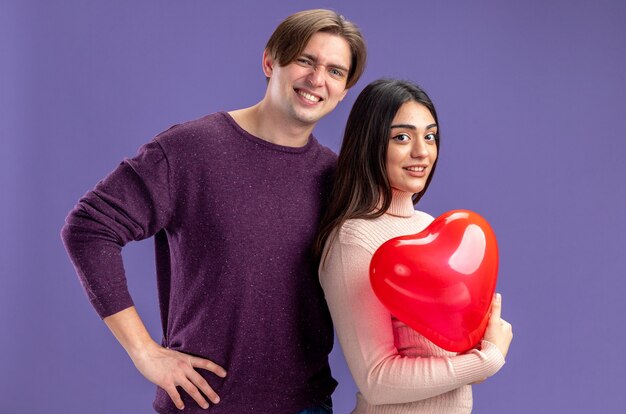 Giovane coppia il giorno di san valentino sorridente ragazzo in piedi accanto alla ragazza con palloncino cuore isolato su sfondo blu