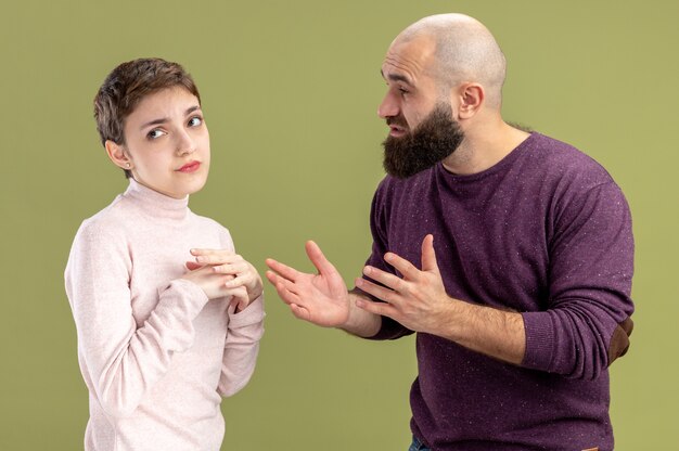 giovane coppia in abiti casual uomo barbuto chiedendo perdono la sua fidanzata confusa concetto di San Valentino in piedi sopra la parete verde