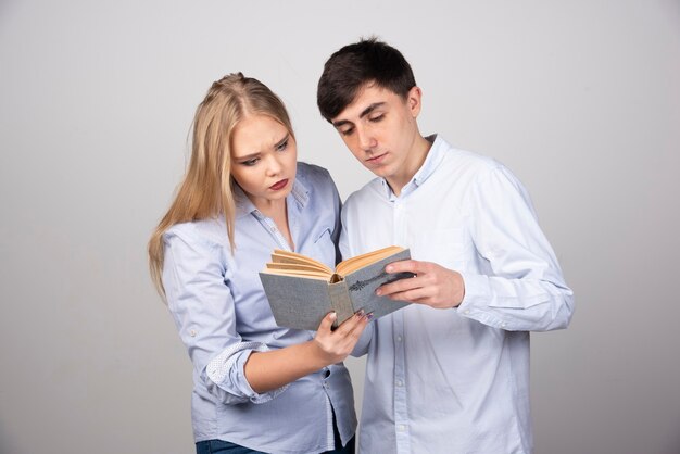 Giovane coppia in piedi con libro su sfondo grigio