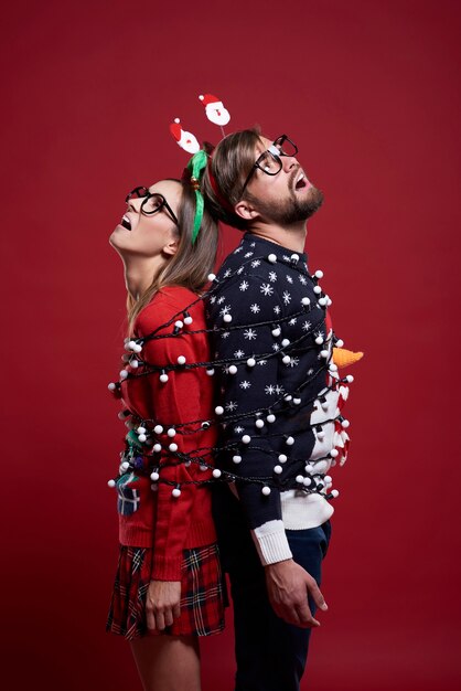 Giovane coppia in strani vestiti di Natale legati con luci di Natale