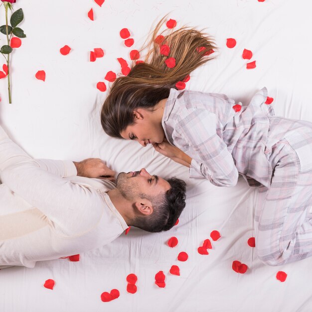Giovane coppia sdraiata a letto con petali di rosa