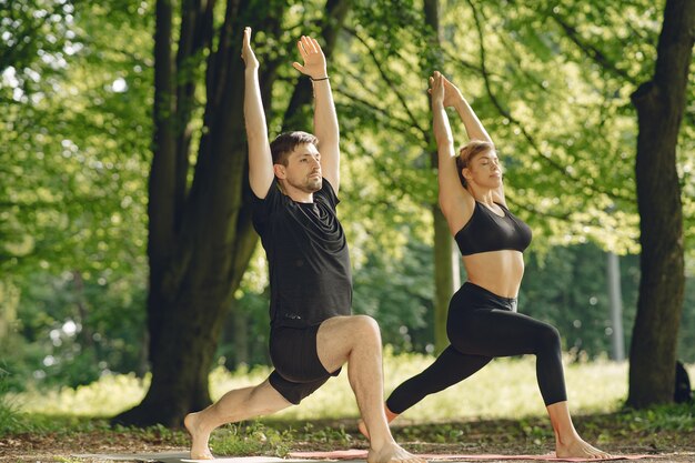 Giovane coppia sportiva facendo yoga fitness. Persone in un parco estivo.