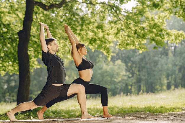 Giovane coppia sportiva facendo yoga fitness. Persone in un parco estivo.