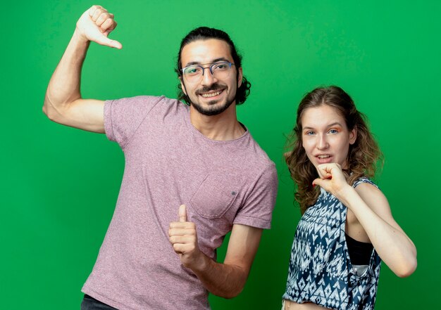 giovane coppia uomo e donna, felice e positivo che punta a se stessi in piedi oltre il muro verde