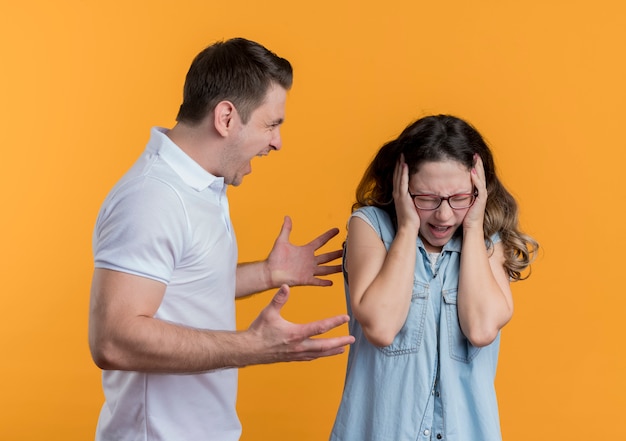 Giovane coppia uomo e donna in abiti casual arrabbiato che grida alla sua ragazza confusa sull'arancio