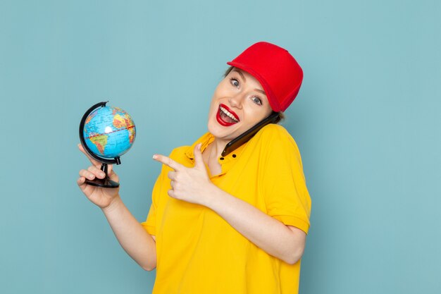 Giovane corriere femminile di vista frontale in camicia gialla e mantello rosso che parla sul telefono che sorride sullo spazio blu