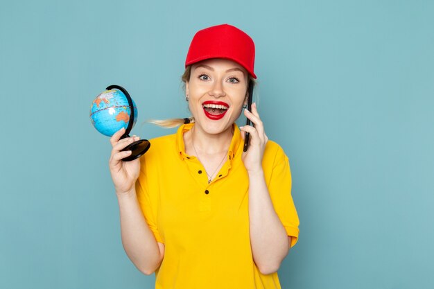 Giovane corriere femminile di vista frontale in camicia gialla e mantello rosso che parla sul telefono che sorride sullo spazio blu