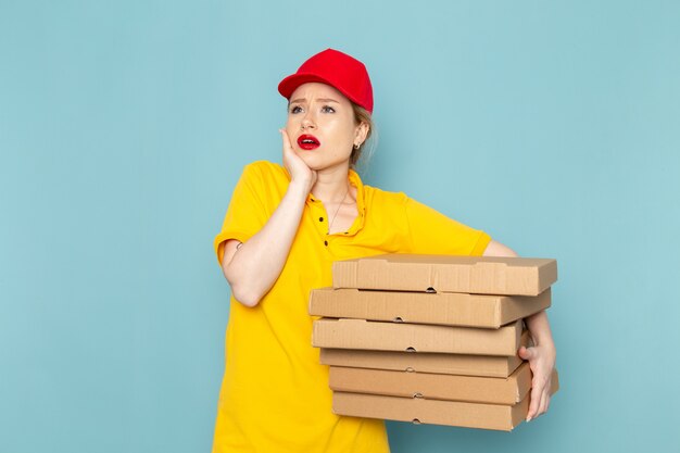 Giovane corriere femminile di vista frontale in camicia gialla e mantello rosso che tiene i pacchetti sullo spazio blu