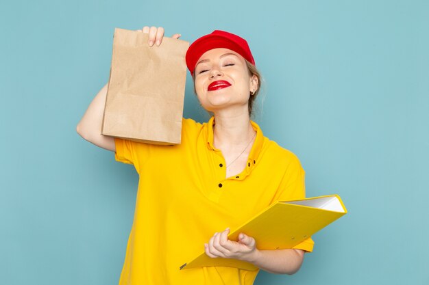 Giovane corriere femminile di vista frontale in camicia gialla e pacchetto rosso della tenuta del capo e archivio giallo che sorride sull'operaio blu dello spazio