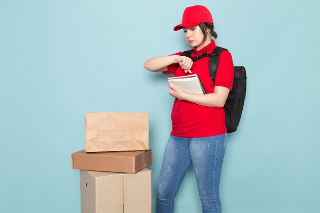 giovane corriere in polo rosso berretto rosso zaino nero tenendo quaderno pacchetto su blu