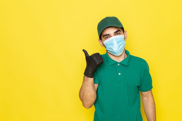 Giovane corriere maschio di vista frontale in guanti neri del cappuccio di verde della camicia verde showign impressionante segno su colore giallo