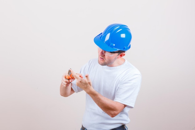 Giovane costruttore che ha il dito con le pinze in maglietta, casco e sembra concentrato