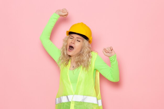 Giovane costruttore femminile di vista frontale nel casco verde del vestito della costruzione che sbadiglia sul lavoro della signora del lavoro di costruzione di architettura dello spazio rosa