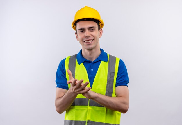 Giovane costruttore uomo che indossa la costruzione uniforme e casco di sicurezza applaude felice