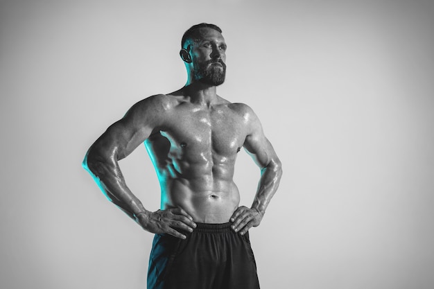 Giovane culturista caucasico formazione su sfondo studio in luce al neon. Modello maschio muscoloso che riposa dopo esercizi di cross-fit. Concetto di sport, bodybuilding, stile di vita sano, movimento e azione.