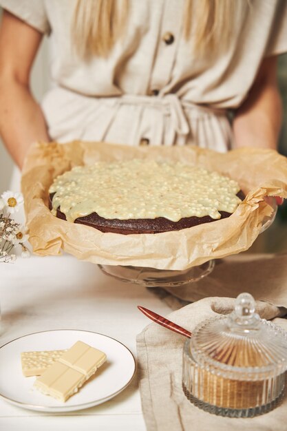 Giovane cuoca che prepara una deliziosa torta al cioccolato con crema su un tavolo bianco