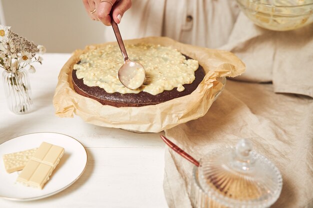 Giovane cuoca che prepara una deliziosa torta al cioccolato con crema su un tavolo bianco